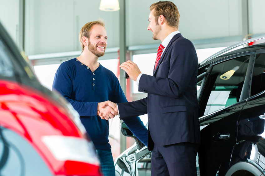 Young man and seller with auto in car dealership